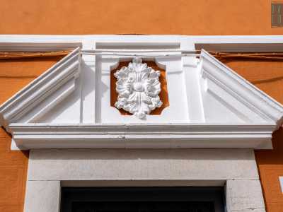 ...impreziosito da un timpano spezzato con al centro un decoro floreale. Dopo una recente ristrutturazione appare oggi di color rosso, mentre fino a poco tempo fa era tinteggiata di verde